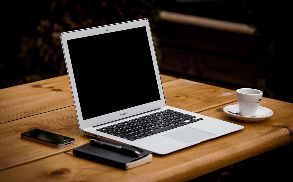 A laptop, notebook, and coffee cup arranged on a wooden table